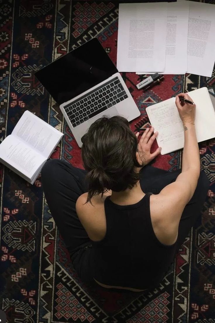 Writing by hand beside a laptop and open books